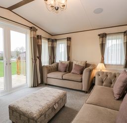 A living room with two sofas an ottoman a lamp and windows with curtains at Hudson's Hideaway in South Lakeland Leisure Village
