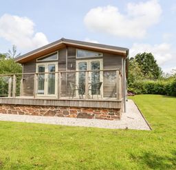 A wooden cabin with glass doors and a small deck with two chairs and a table in a grassy yard at 6 Southern Place in Dobwalls