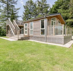 A wooden cabin with an outdoor staircase and glass railings surrounded by grass and trees at 4 Faraway Fields in Dobwalls