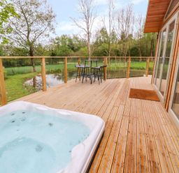 A wooden deck with a hot tub table and chairs overlooking a pond and trees at 21 Meadow Retreat in Dobwalls