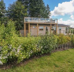 A wooden house with a glass balcony and garden with flowering shrubs at 2 Southern Place in Dobwalls