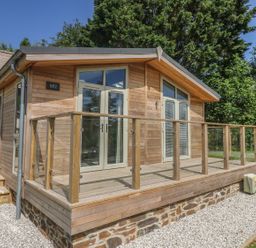 A wooden cabin with glass doors and a glass railing deck surrounded by gravel and trees at 2 Southern Place in Dobwalls