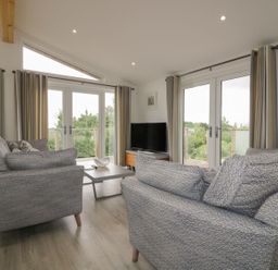 A living room with two gray sofas a coffee table a TV on a wooden stand and large windows at 7 Faraway Fields in Dobwalls