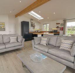 A living room with two gray sofas facing a coffee table and an open kitchen with wooden counters and cabinets at 7 Faraway Fields Dobwalls