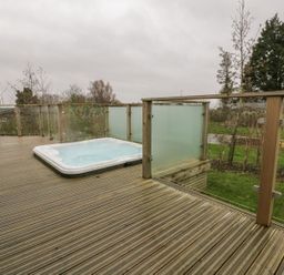 An outdoor deck with a hot tub and glass railings overlooking a garden at 7 Faraway Fields in Dobwalls
