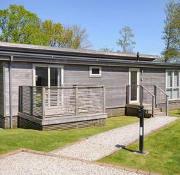 A wooden cabin with a small porch and gravel pathway surrounded by grass and trees at 19 Meadow Retreat in Dobwalls
