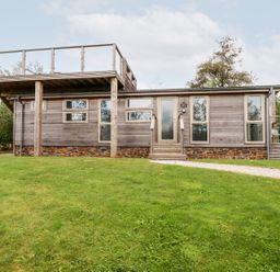 A single story wooden house with a deck and rooftop terrace on a grassy lawn at 1 Southern Place in Dobwalls