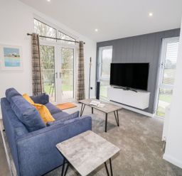 A living room with a blue sofa yellow cushions coffee table TV on wall unit and patio doors at 1 Southern Place in Dobwalls