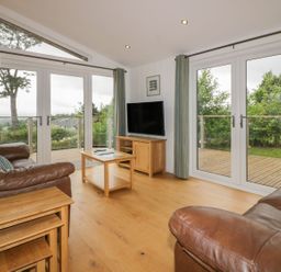 A living room with leather sofas wooden tables a television and large glass doors opening to a deck at 11 Faraway Fields Dobwalls