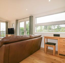 A living room with a brown leather sofa a wooden desk with a lamp and stool and large windows at 11 Faraway Fields in Dobwalls