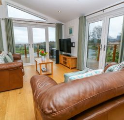 A living room with two brown leather sofas a wooden coffee table a TV on a wooden stand and large windows at 12 Faraway Fields in Dobwalls