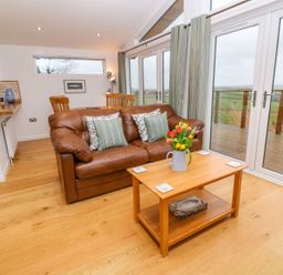 A living room with a brown leather sofa two pillows wooden coffee table with flowers and dining table with chairs at 12 Faraway Fields in Dobwalls