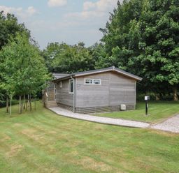 A wooden cabin surrounded by grass and trees at 24 Meadow Retreat Dobwalls