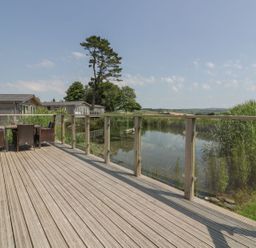 A wooden deck with outdoor furniture next to a pond and other houses visible in the background at 15 Faraway Fields in Dobwalls