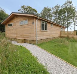 A wooden cabin with windows and a gravel path in a grassy area at 18 Meadow Retreat in Dobwalls