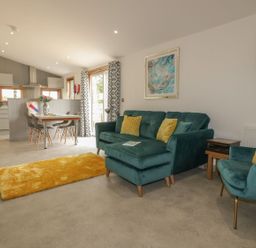 A living room with teal sofa and armchair with yellow cushions and dining table with chairs at 18 Meadow Retreat in Dobwalls