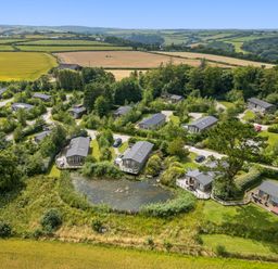 Aerial view of a rural estate with several cabins around a pond and fields in the background at 18 Meadow Retreat in Dobwalls