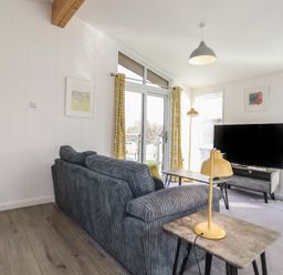 A living room with a gray sofa yellow lamps a television on a stand and glass doors with yellow patterned curtains at 11 Meadow Retreat in Dobwalls