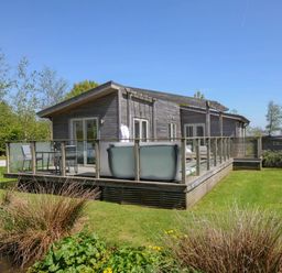 A wooden cabin with a glass railing deck and outdoor seating on a lawn with trees and shrubs at 11 Meadow Retreat in Dobwalls