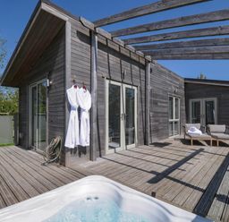 An outdoor wooden deck with two white bathrobes hanging on a wall a hot tub chairs and a table at 11 Meadow Retreat in Dobwalls