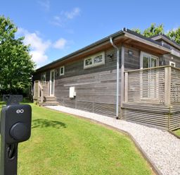 A wooden cabin with a deck and electric vehicle charger at 12 Meadow Retreat in Dobwalls