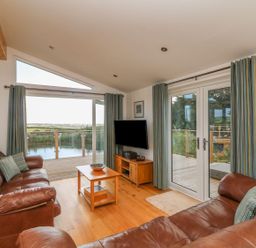 A living room with leather sofas coffee table and a TV with a view of a deck and countryside at 14 Faraway Fields in Dobwalls