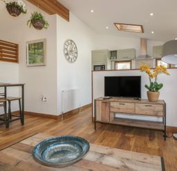 A living area with a wooden floor a television on a wooden stand a floor lamp and a dining table with two benches at 9 Meadow Retreat in Dobwalls