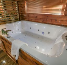 A white jacuzzi tub with chrome faucets and controls in a wooden room with window blinds and a towel hanging on the edge at 9 Meadow Retreat in Dobwalls