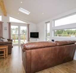 A living room with brown leather sofas wooden nesting tables and a television at 7 Meadow Retreat in Dobwalls
