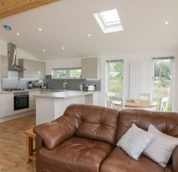 An open kitchen and dining area with a brown sofa in the foreground at 7 Meadow Retreat in Dobwalls