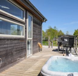 An outdoor wooden deck with a hot tub and a table with chairs at 7 Meadow Retreat in Dobwalls