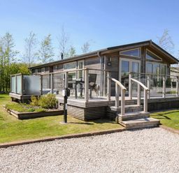A wooden cabin with a glass railing deck and steps on a grassy lawn at 7 Meadow Retreat in Dobwalls