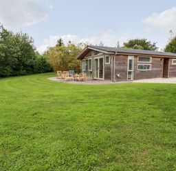 A wooden house with a patio and outdoor furniture on a large grassy lawn surrounded by trees at 14 Horizon View in Dobwalls