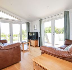 A living room with two brown leather sofas facing a TV and large glass doors at 5 Meadow Retreat in Dobwalls