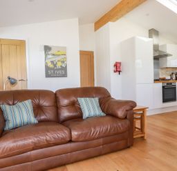 A brown leather sofa with striped pillows and a kitchen with white cabinets and wooden floors at 5 Meadow Retreat in Dobwalls