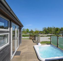 An outdoor wooden deck with a hot tub next to a building and glass railing at 5 Meadow Retreat in Dobwalls