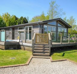 A wooden house with glass railings on a deck and a gravel pathway leading to stairs at 5 Meadow Retreat in Dobwalls