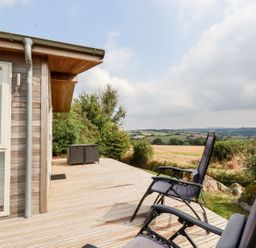 An outdoor wooden deck with two reclining chairs and storage boxes overlooking fields and hills at 11 Horizon View in Dobwalls
