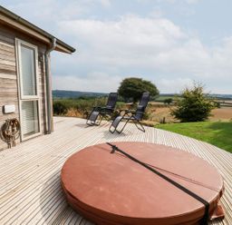 A wooden deck with two black reclining chairs and a covered circular hot tub next to a house in Dobwalls