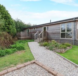 A wooden house with a gravel pathway and garden at 2 Meadow Retreat in Dobwalls