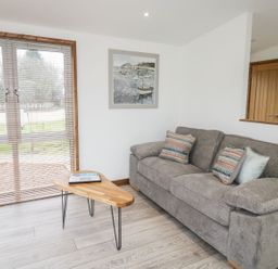 A living room with a grey sofa and wooden coffee table near window blinds at 2 Meadow Retreat in Dobwalls