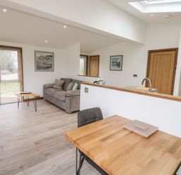 An open living and dining area with a gray sofa and wooden dining table at 2 Meadow Retreat in Dobwalls