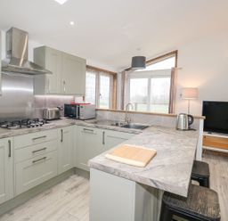 A kitchen with gray cabinets and marble countertops next to a living area with a television at 2 Meadow Retreat in Dobwalls