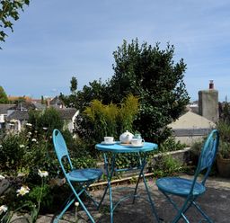 A patio with a blue metal table and two chairs with a teapot and cups surrounded by plants at 30 Sherborne Lane in Lyme Regis