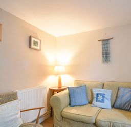 A living room with a beige sofa with blue cushions a patterned armchair and a lamp on a side table at 30 Sherborne Lane in Lyme Regis