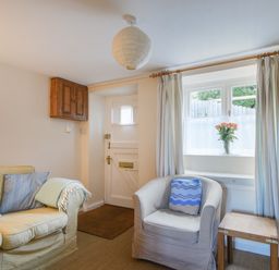 A small living room with a beige sofa and armchair a wooden side table and a window with flowers on the sill at 30 Sherborne Lane in Lyme Regis