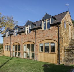 A two story stone and brick house with multiple windows and an exterior stone staircase with a lawn at The Granary in Little Dasset near Gaydon