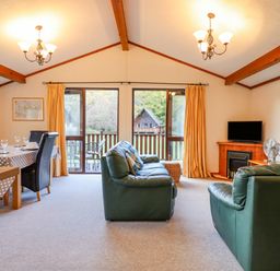 A living room with green leather sofas a dining table with chairs and large windows overlooking a garden at Dartmoor Retreat Lodge in Clifford Bridge near Moretonhampstead