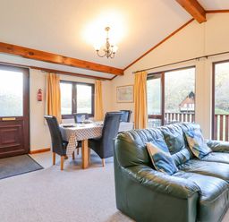 A living room with a green leather sofa, dining table with black chairs, and large windows at Dartmoor Retreat Lodge Clifford Bridge near Moretonhampstead