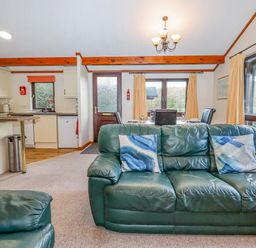 An open living room and kitchen with green leather sofas a dining table and windows at Dartmoor Retreat Lodge in Clifford Bridge near Moretonhampstead